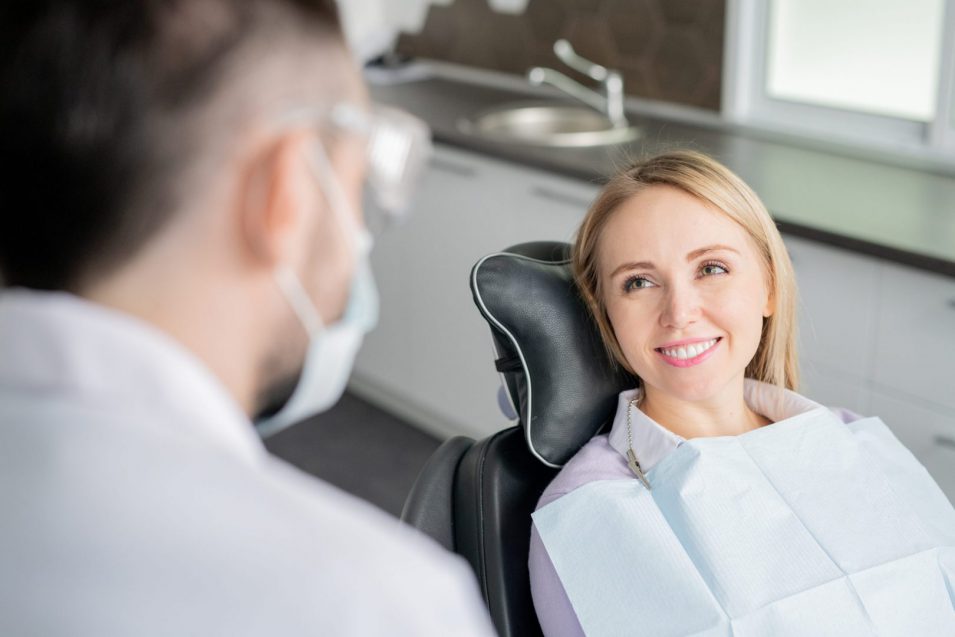 Happy young blonde female patient looking at her dentist with healthy smile Happy young